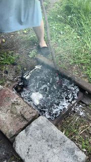 Разгоревшиеся угли в самодельном мангале, вокруг пепел и дым, видно рабочее место на земле в саду — атмосфера деревенского очага.