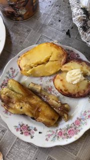 Порция готовой деревенской еды: запечённая картошка с маслом и кусочки баклажана на тарелке, поданные на столе на свежем воздухе.