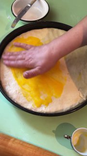Смазка верхнего слоя теста чем-то желтоватым (вероятно желток) перед запеканием; руки разравнивают поверхность.