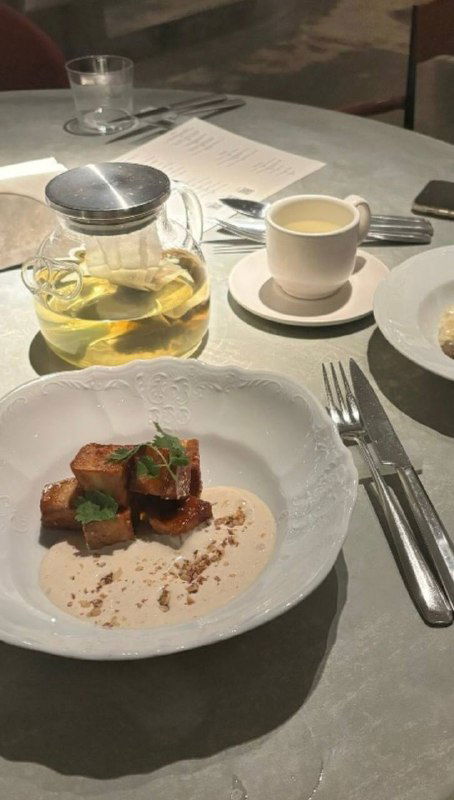 Порция с кусочками и кремовым соусом на белой тарелке, рядом приборы и чайник — крупный план эстетичной сервировки в Soma