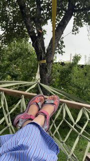 Ноги в сандалиях в гамаке под деревом: расслабленная поза, вид на сад и полотно гамака, тёплая летняя атмосфера отдыха на даче.
