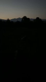 Тёмный снимок заката: силуэты деревьев и гор на горизонте, наступающая ночь и приглушённые оттенки вечера в деревне.