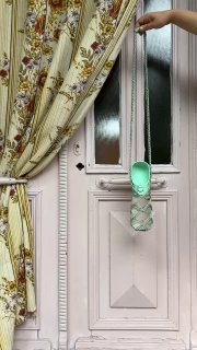 Самодельный вязаный чехол для бутылки, подвешенный у дверного проёма — простая рукодельная деталь быта и домашнего уюта в деревне.