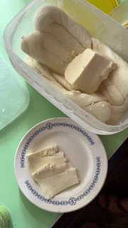 Контейнер с домашним белым сыром и куски сыра на тарелке рядом — простая молочная еда, похожая на творог или домашний сыр.