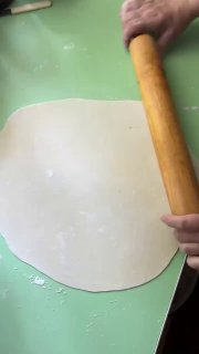 Руки раскатывают тонкий лист теста на зелёной рабочей поверхности — начало приготовления татар бераги в домашней кухне, кадр процесса.