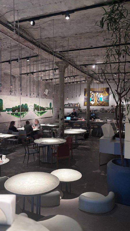 Интерьер ресторана Soma: широкий зал с индустриальным потолком, столами, стульями и картинами на стенах в мягком свете