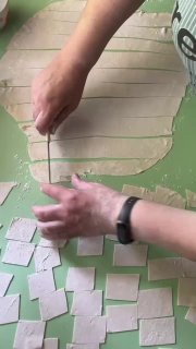 Нарезка теста на ровные полоски и последующее нарезание квадратиков — подготовка кусочков для варки татар бераги, вид сверху рук и теста.