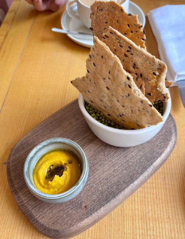 Подача мезе: хрустящие крекеры на деревянной доске и мисочка с горчично-жёлтой пастой, аккуратная сервировка на столе ресторана.