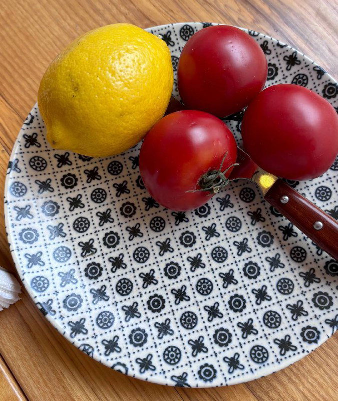 Тарелка с большим лимоном и тремя яркими помидорами-черри на узорчатой тарелке; простая летняя композиция на столе ресторана.