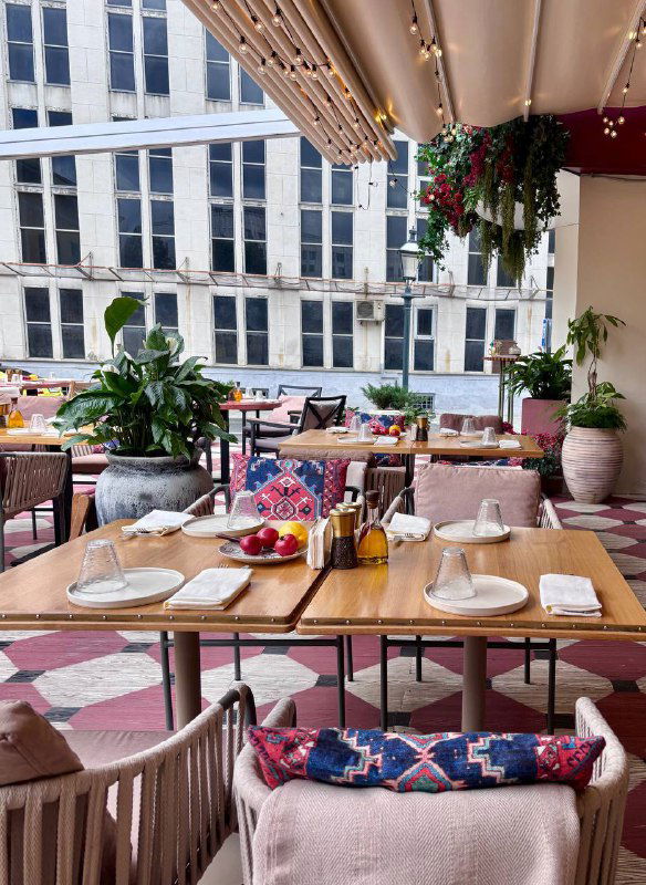 Терасса или зона у окна ресторана Mouflon: столики с сервировкой, подушки на стульях и вид на город — лёгкая летняя атмосфера.