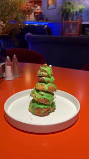 Небольшая новогодняя елочка из профитролей с зелёной помадкой на белой тарелке — десертная акция в декабрьском меню Скворца