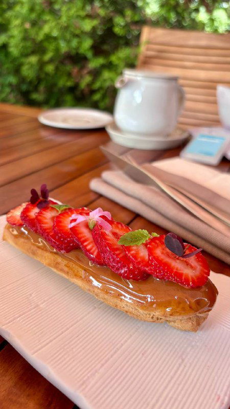 Длинный эклер с ягодами на тарелке на фоне столовой посуды — яркий ягодный декор и тонкая глазурь на десерте.