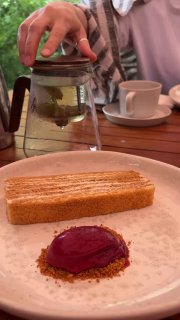 Подача десерта и рук официанта с чайником на заднем плане — кадр отражает атмосферу сервиса и тёплую обстановку на веранде.