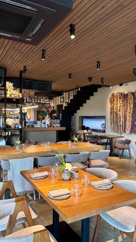 Интерьер ENO Bistro: столы, деревянные панели, тёплое освещение и уютная современная обстановка ресторана с видом на зал.