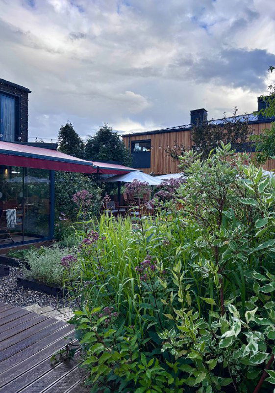 Открытая веранда и густые зелёные кусты вокруг столов на свежем воздухе — место для ужина среди растений и спокойной атмосферы.