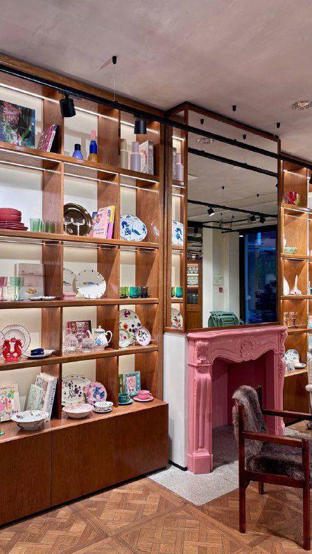Интерьер кофейни при магазине Nuself: полки с посудой, розовый камин и кресло в уютной зоне для сидения, пастельная уютная атмосфера.