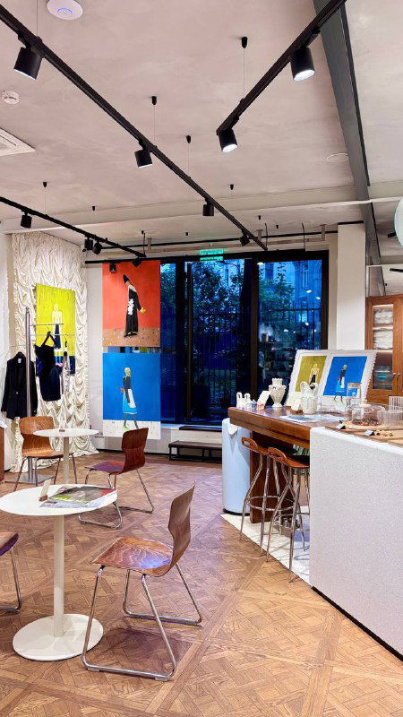 Общий вид интерьера кофейни при магазине Nuself: столы, стулья и настенные картины, просторное помещение с дизайнерской отделкой и теплыми цветами.