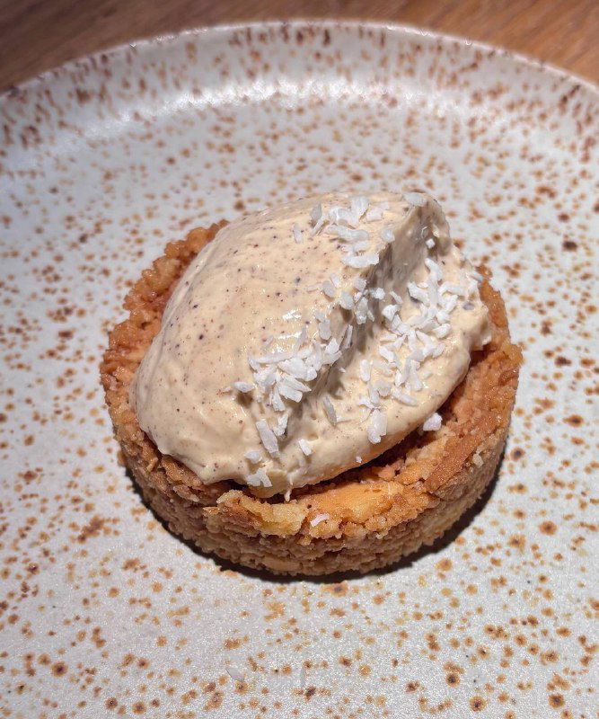 Небольшой десерт: корж с кремом и кокосовой стружкой на тарелке — фотография финального блюда ужина в Tacobar