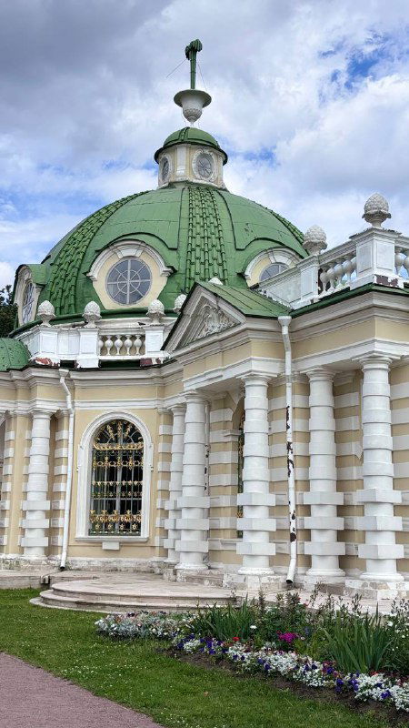 Фасад паркового павильона Кусково с зелёной куполообразной крышей, белыми колоннами и цветочной клумбой у входа — вид снаружи усадьбы.