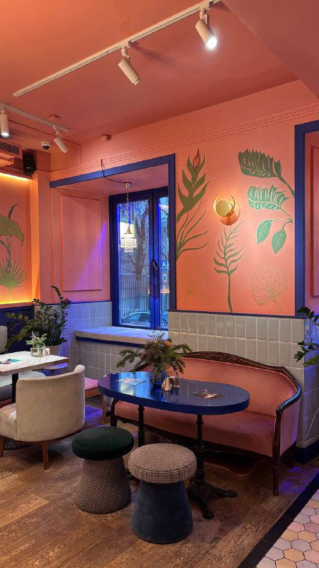 Розово-голубой интерьер кафе с картинами на стенах, столиками и пуфами — атмосфера в духе режиссера Уеса Андерсона в Скворце