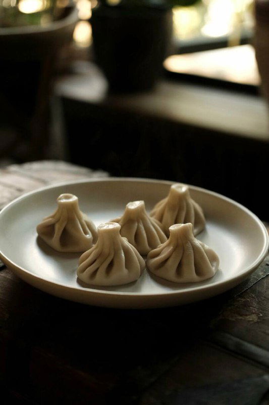 Тарелка с пятью аккуратно слепленными хинкали на тёмном фоне, видно складки теста и пышную форму, вид сбоку.