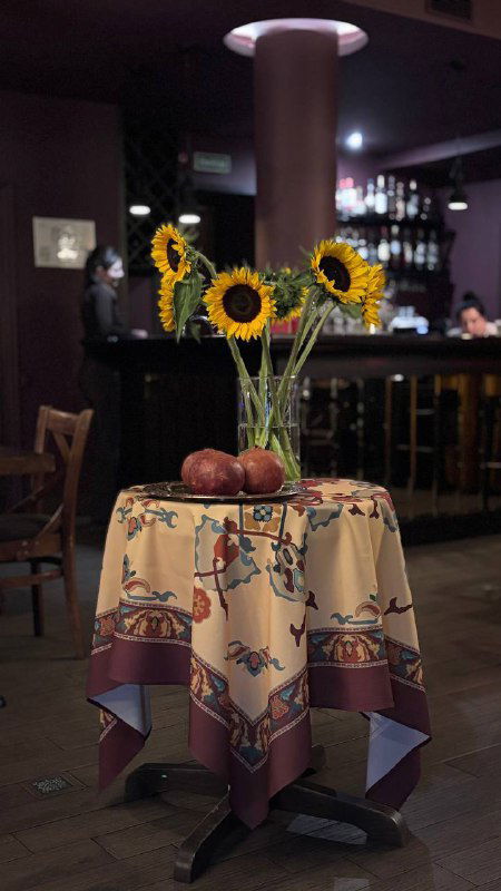 Небольший столик с подсолнухами и гранатами на скатерти в армянском стиле — декоративный элемент в зале ресторана.