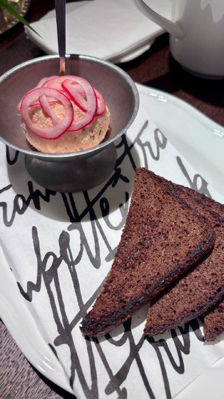 Закуска в маленькой кастрюльке с маринованным луком и ломтиком тёмного хлеба на тарелке — текстура и сервировка бистро.