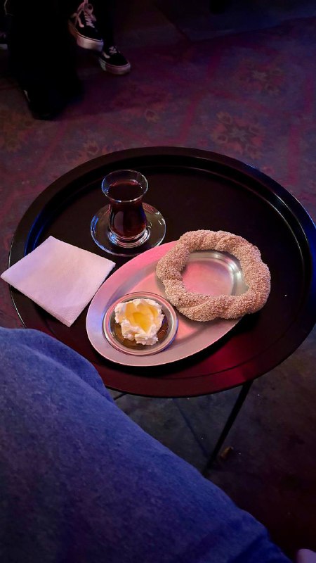 Крупный план подачи: симит с кунжутом, мисочка каймака с медом и стакан чая на круглом подносе, уютный тёплый кадр.