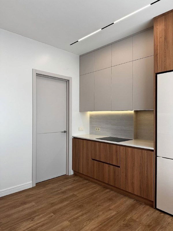 Кухонная зона с дверью LINE 10: однотонная светлая дверь рядом со встроенной мебелью и подсветкой, пример сочетания дверного полотна с кухонным интерьером.