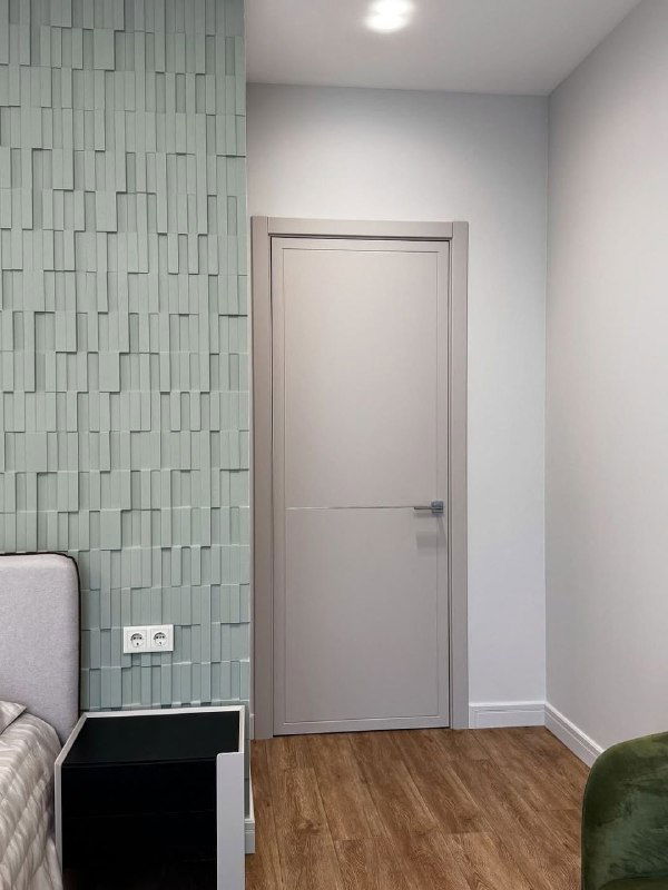 Дверь LINE 10 у фактурной плиточной стены в спальне: нейтральное полотно, тумбочка и мягкая зона, показывающие, как дверь вписывается в интерьер по цвету и текстуре.