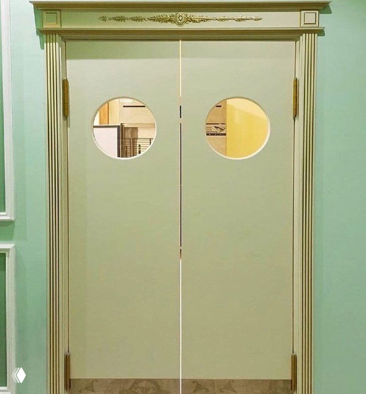 Светло-зелёные маятниковые двери с круглыми окнами и декоративной резьбой вокруг проёма: интерьер в классическом стиле, демонстрация варианта наличников и отделки.