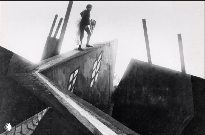 Силуэт фигуры на крыше на фоне искажённой перспективы и острых линий архитектуры, подчёркивающей тревожность сюжета.