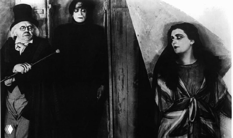 Персонажи в дверном проёме, свет и тень создают сценическую композицию; кадр демонстрирует стилистику экспрессионизма в фильме.