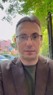 Портрет мужчины в очках и пиджаке на уличном фоне с деревьями и домами — фото для анонса профессионального вебинара.
