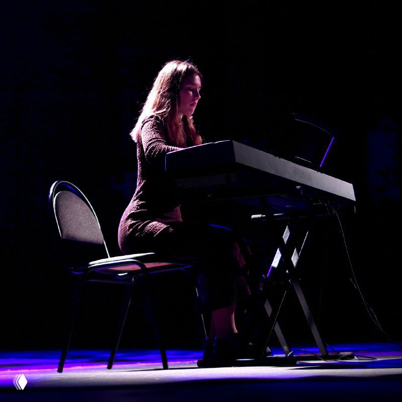 Пианистка за электронным фортепиано в зале выступает с концертным номером, спокойный кадр, фокус на руках и инструменте на сцене.