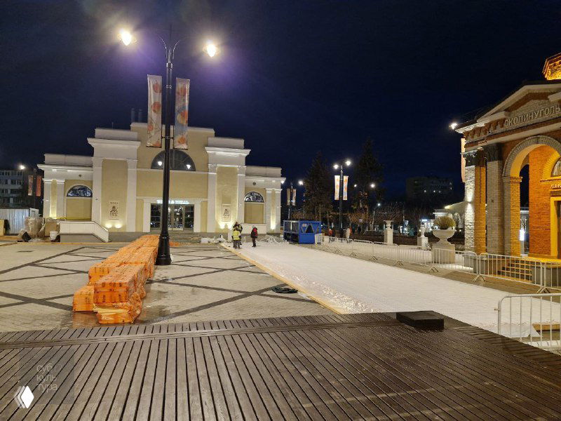 Ночная площадь на территории ВДНХ в Рязани: деревянные настилы, ограждения и подготовка поверхности под каток в предновогодний вечер при уличном освещении.