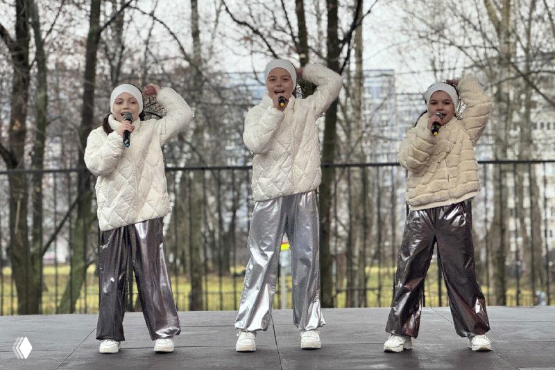 Три юные исполнительницы в белых куртках исполняют номер на уличной сцене Рязани в рамках праздничной программы открытия для детей и семей.