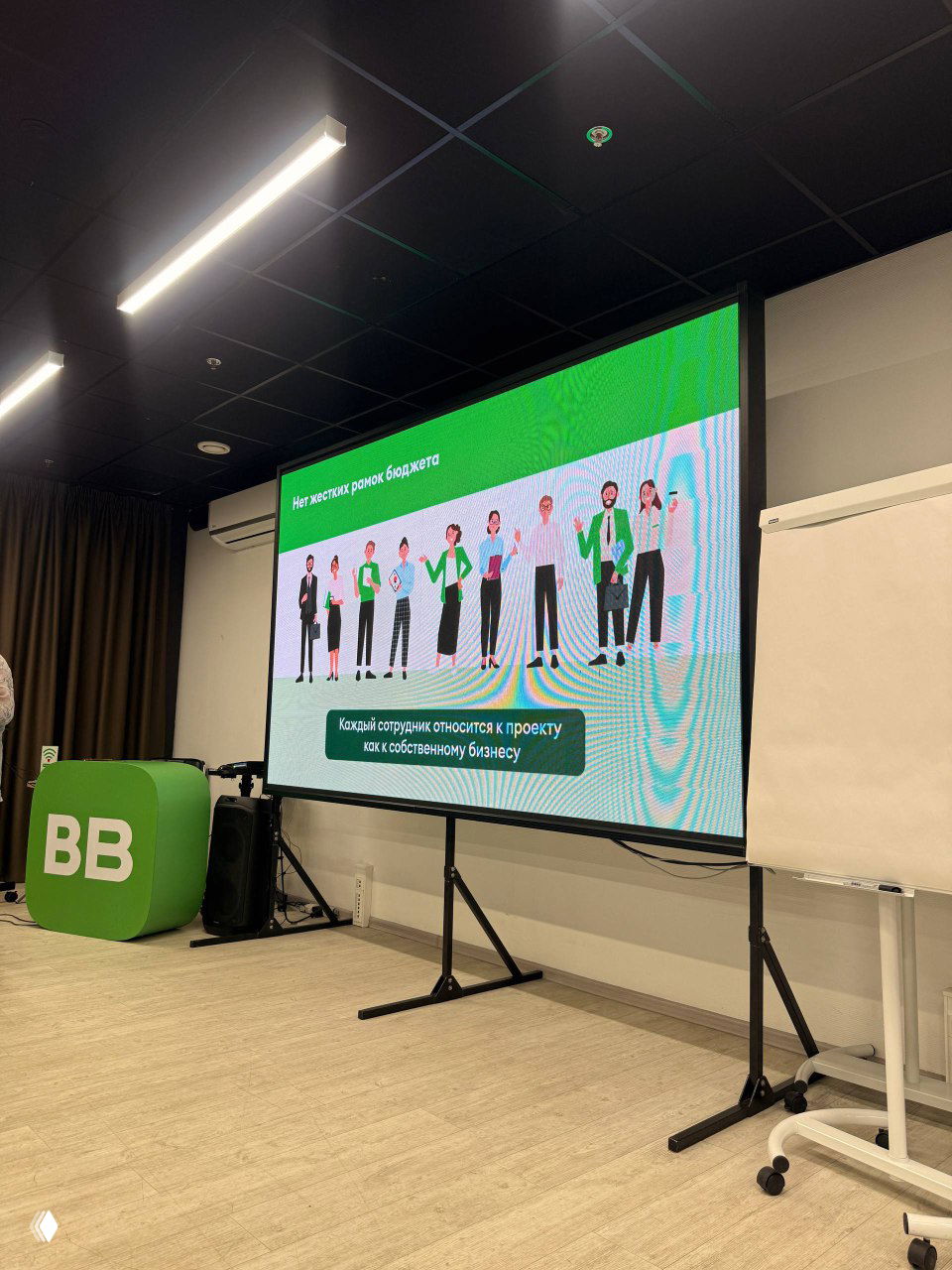 Широкий кадр экрана с слайдом о проектной структуре и надписью про отношение сотрудников к проекту как к собственному бизнесу; видна брендовая стойка с буквами BB.