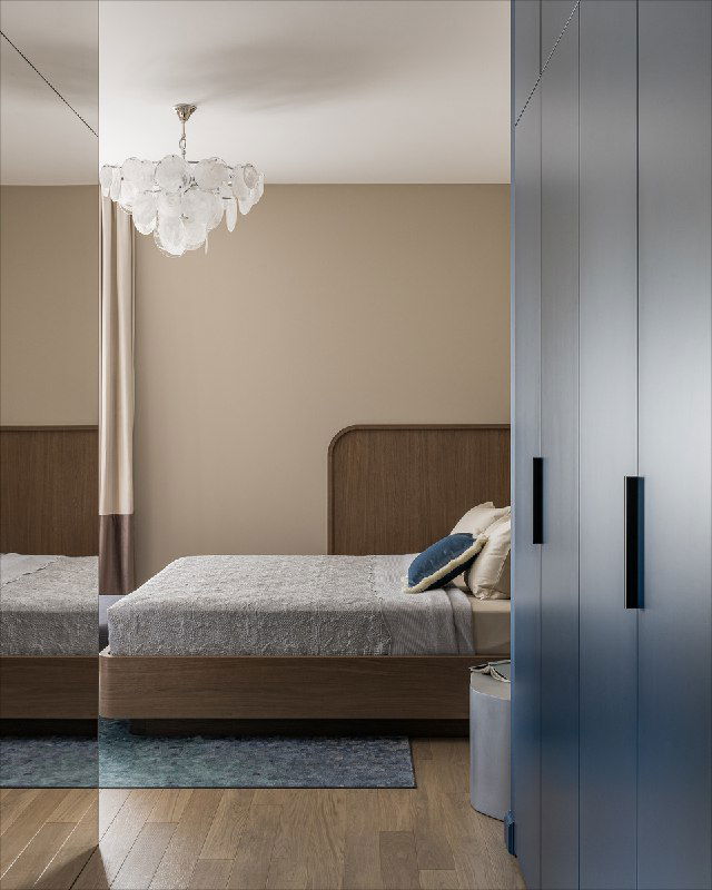 Вид в приватную зону квартиры: справа глубокие синие фасады шкафа, слева нейтральная спальня с мягкой кроватью, деревянный пол и приглушённая палитра в интерьере.