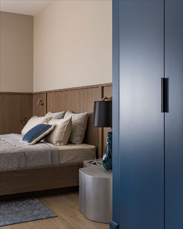 Вертикальный кадр кровати и синих шкафов: текстиль, декоративные подушки и окрашенная панель из шпонированного МДФ в мягких бежево‑голубых тонах проекта.