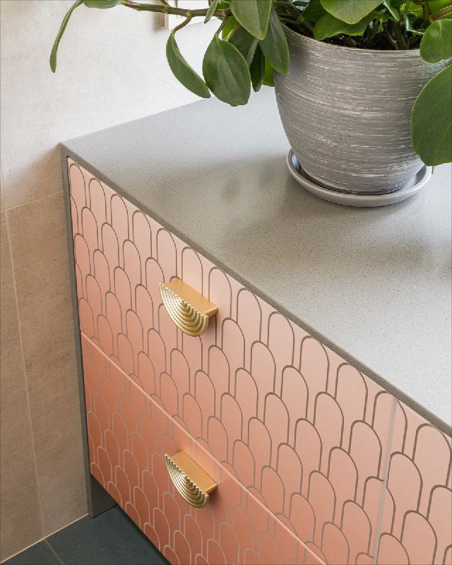 Деталь тумбы в ванной с градиентной цветной печатью фасадов и золотистыми ручками; на столешнице виден текстурный искусственный камень и декоративный горшок.