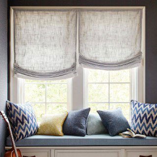 Подоконная зона с мягким сиденьем и подушками, над ней полупрозрачные светлые римские шторы, создающие уютное место для чтения.