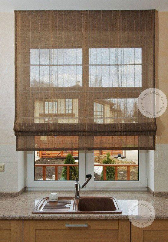 Кухонное окно с коричневыми тканевыми римскими шторами; опущенные шторы демонстрируют фактуру и тёплые оттенки древесины на фоне.