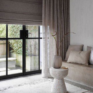 Современная гостиная с большими окнами и бежевыми римскими шторами в сочетании с длинными шторками; натуральные текстуры и мягкие ткани.