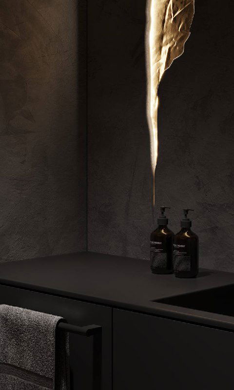 Крупный план чёрной столешницы и раковины в графитовом санузле с фактурной тёмной стеной, бутылочками и вертикальным светящимся элементом-«трещиной».
