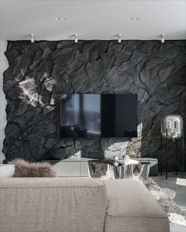 Рельефное панно под натуральный камень тёмно-серого тона за телевизором; видна текстура камней и контраст с мягкой мебелью в гостиной.