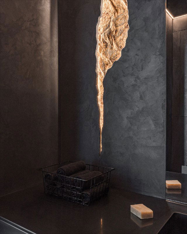 Крупный план интерьерного светильника‑панно: золотая текстура врезана в стену на фоне тёмной декоративной отделки и светодиодной подсветки.