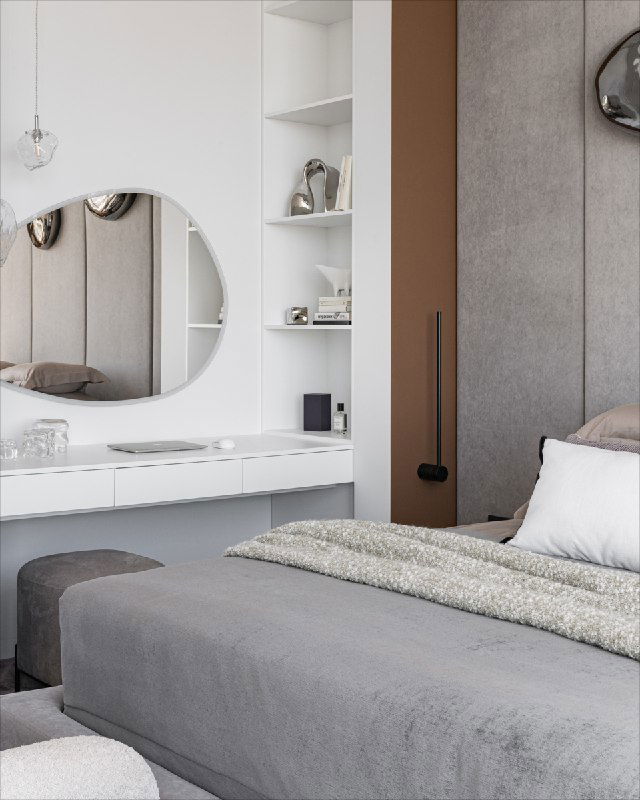 Угол спальни с белым макияжным столиком и круглым зеркалом, рядом видна часть кровати и отделка стены с декоративными элементами в спокойной цветовой гамме.