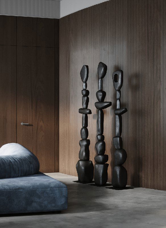 Полукруглая рейковая стена и три высокие абстрактные скульптуры‑тотемы тёмного тона, расположенные как арт-объекты на фоне древесных панелей интерьера.