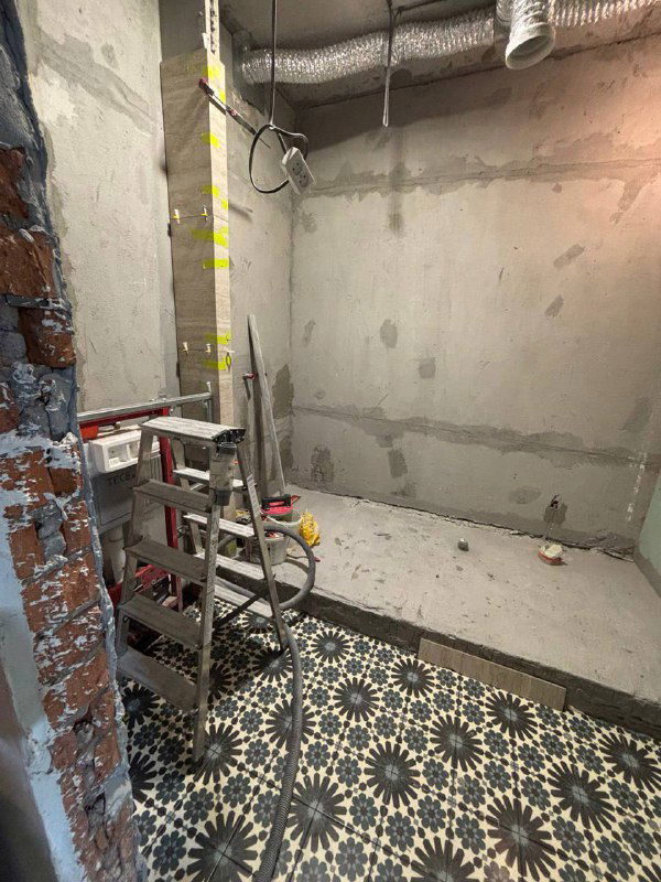 Фото мокрой зоны на этапе ремонта: подготовленный пол с уложенной узорчатой плиткой и строительные работы под дальнейшую отделку ванной комнаты.